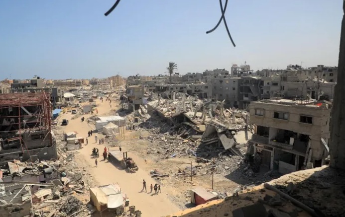 فلسطينيون يسيرون في شارع وسط المباني المدمرة في مدينة خان يونس جنوبي قطاع غزة